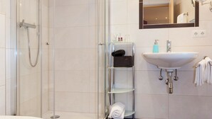 A modern bathroom with a glass shower enclosure, a white sink, and a mirror above the sink. - Cozy vacation apartment and perfect base in the heart of Tyrol (Inzing)