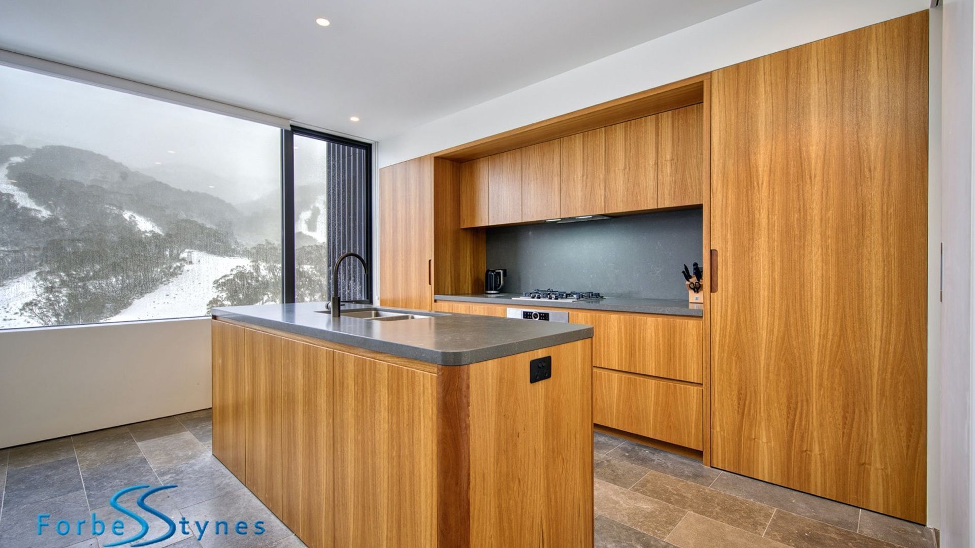Una cocina moderna con armarios de madera, una isla central y vistas a un paisaje nevado a través de un ventanal.
