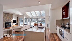 A modern kitchen with a central island, a dining area with a view, and a cozy seating area with a fireplace. - The Peak Penthouse 8 (Central Village)