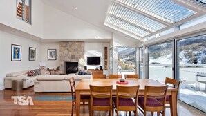 A modern living room with a stone fireplace, a flat-screen TV, and a dining area with wooden chairs. - The Peak Penthouse 8 (Central Village)