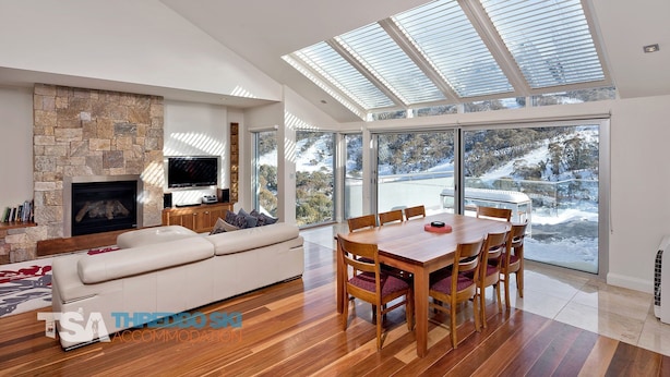 A modern living room with a stone fireplace, a large TV, a sofa, and a dining area with a wooden table and chairs. - The Peak Penthouse 8 (Central Village)