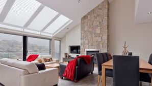 A modern living room with a stone fireplace, a dining area, and a large window with a view.