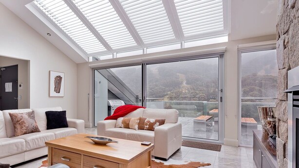 A modern living room with a high ceiling, a glass door leading to a balcony, and a fireplace.