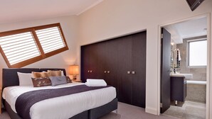 A bedroom with a bed, nightstands, a dark wardrobe, and a bathroom visible through an open door.