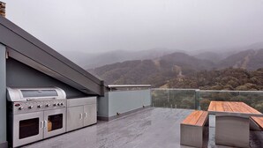An outdoor patio with a barbecue grill and a table, overlooking a mountainous landscape.