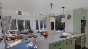 Een moderne keuken met een groot eiland, groene kasten en een zithoek met een bank en salontafel.