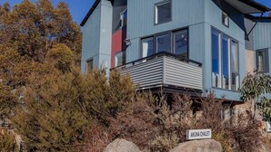 Een modern, twee verdiepingen hoog gebouw met een balkon, omringd door natuurlijke begroeiing en rotsen.