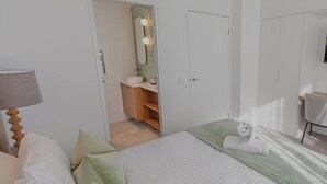 Hotelkamer met een bed, nachtkastje met lamp, bureau met stoel, kledingkast en een badkamer met spiegel en wastafel.