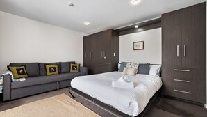 A modern bedroom with a grey sofa, a large bed, and dark wooden wardrobes. - Celesia 2 - Central Village (Central Village)