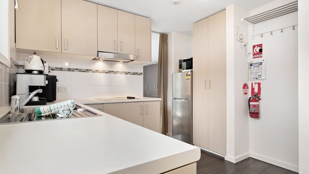 A modern kitchen with light wood cabinets, a stainless steel refrigerator, a coffee machine, and a fire safety sign. - Celesia 2 - Central Village (Central Village)