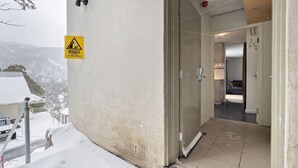 A hotel entrance with a caution sign for falling ice and snow, a glass door, and a view of snow-covered surroundings. - Celesia 2 - Central Village (Central Village)