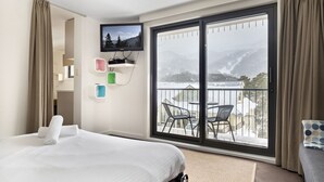 A hotel room with a bed, a TV mounted on the wall, a balcony with chairs, and a view of mountains. - Celesia 2 - Central Village (Central Village)