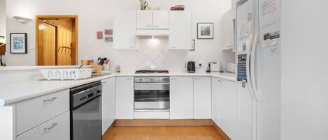 A modern kitchen with white cabinetry, a dishwasher, a stove, and an oven. There are small decorative items on the cabinets and a refrigerator with magnets and notes.