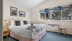 A bedroom with a bed, a nightstand, a window with a view of a building, and a radiator.