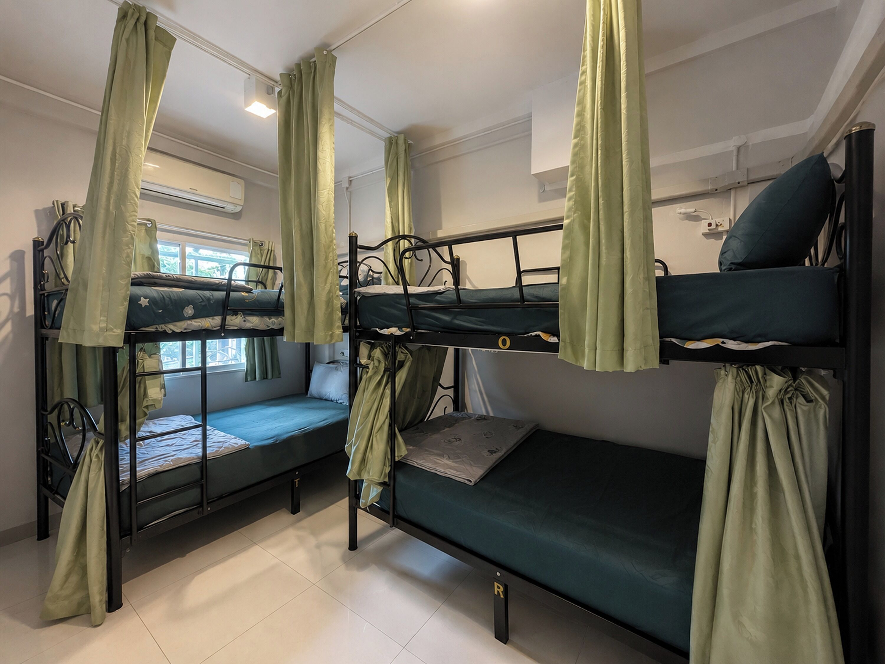 A dormitory room with bunk beds, green curtains, and a window.