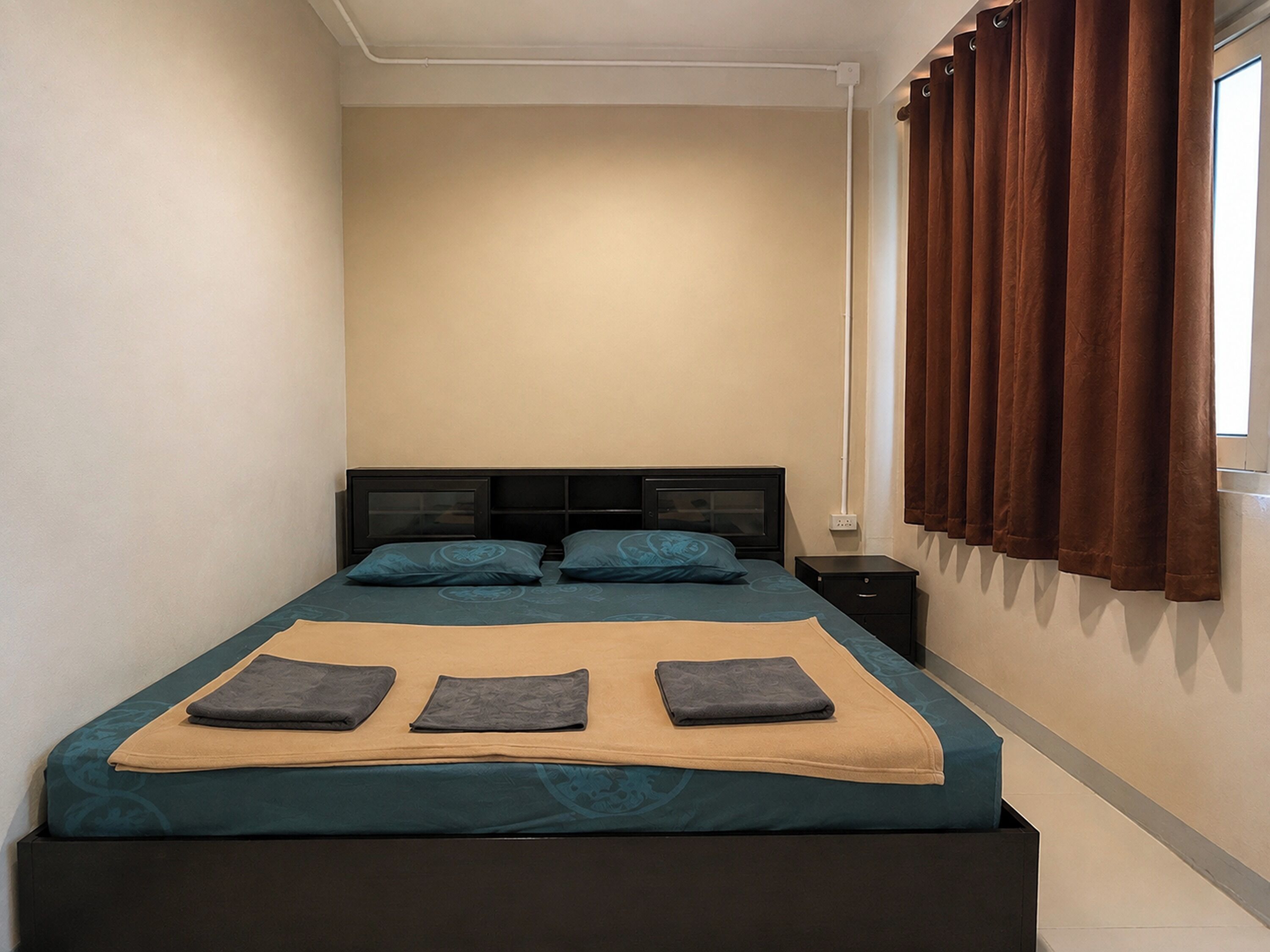 A single bed with a headboard, a bedside table, and a window with curtains.
