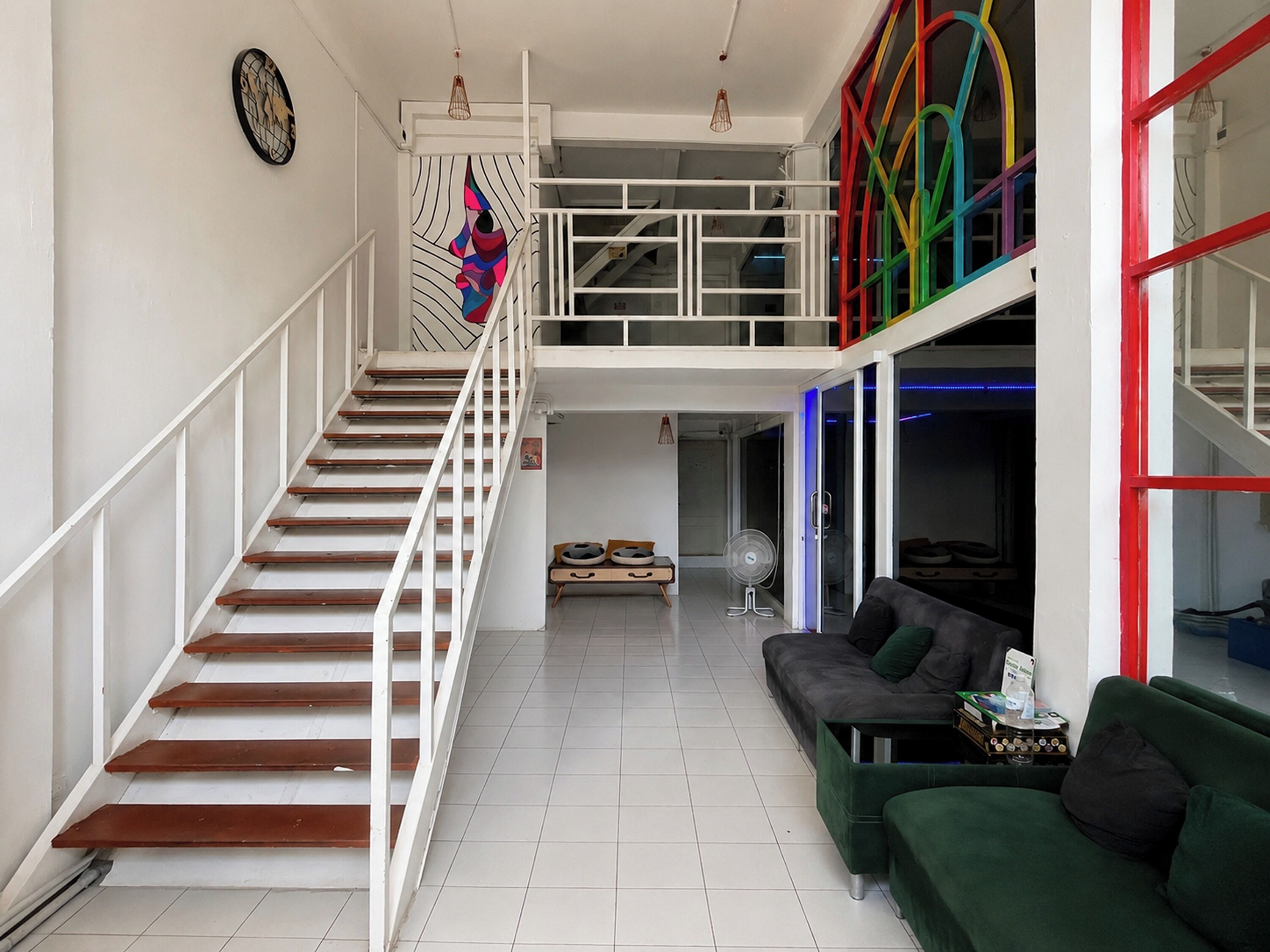 A staircase leading to a second-floor balcony with a colorful railing, a green sofa, and a fan on the floor.