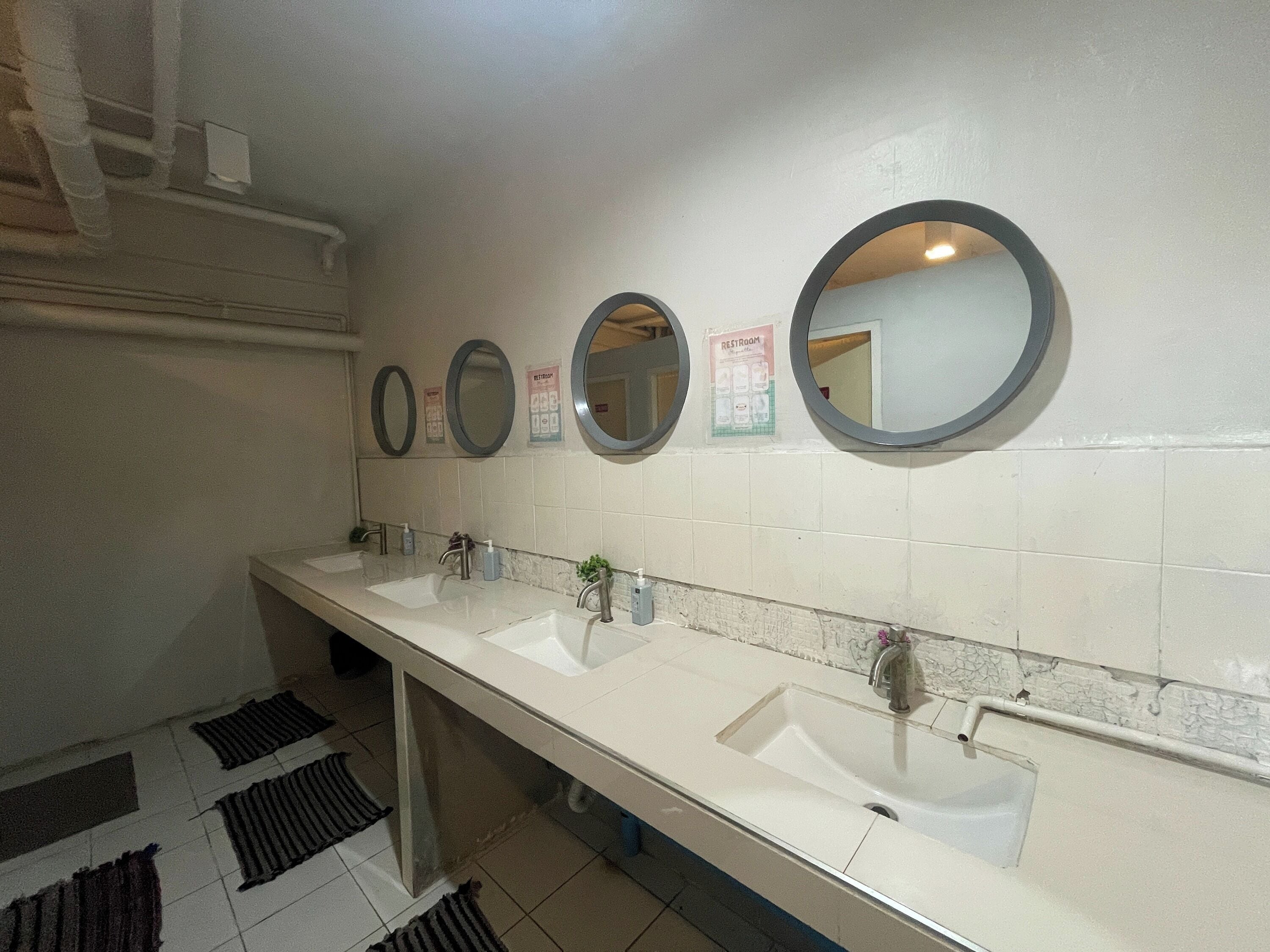 Baño público con tres lavamanos y tres espejos en la pared.