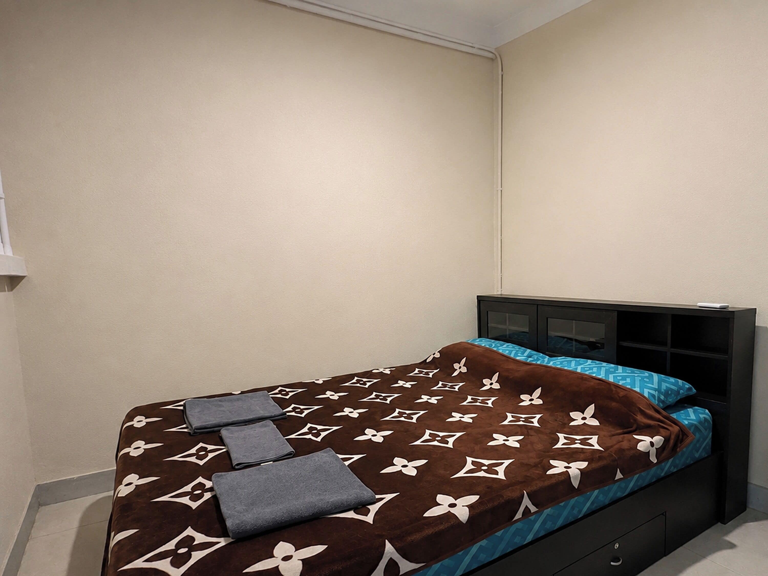 A single bed with a patterned bedspread and pillows, a bedside table, and a wall-mounted TV.
