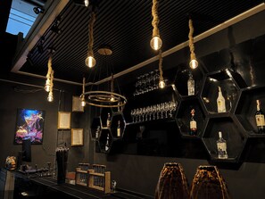 A bar area with hexagonal shelves holding bottles and glasses, a television screen, and a ceiling with exposed beams and hanging lights. - Lemon Tree Khaosan Hostel (Bangkok)