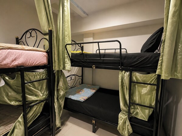 Habitación con literas, cortinas verdes, una cama individual con edredón floral y una litera con colchón negro.