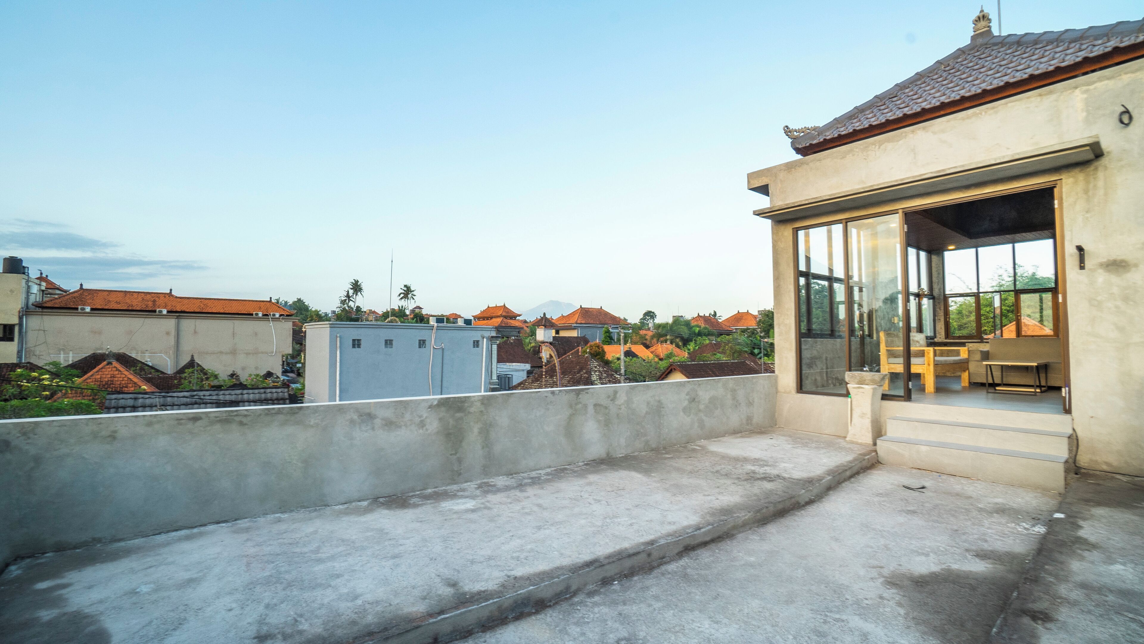 Una terraza en la azotea con suelo de hormigón, una pequeña zona de estar con mesa y sillas, y vistas de edificios circundantes con tejados rojos.