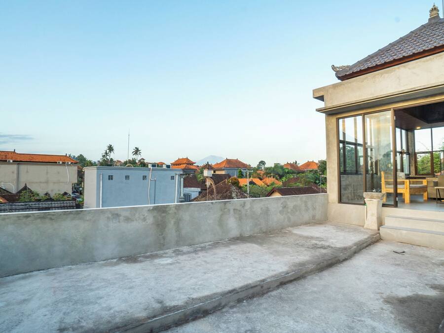 A rooftop terrace with a concrete floor, a small seating area with a table and chairs, and a view of surrounding buildings with red-tiled roofs.