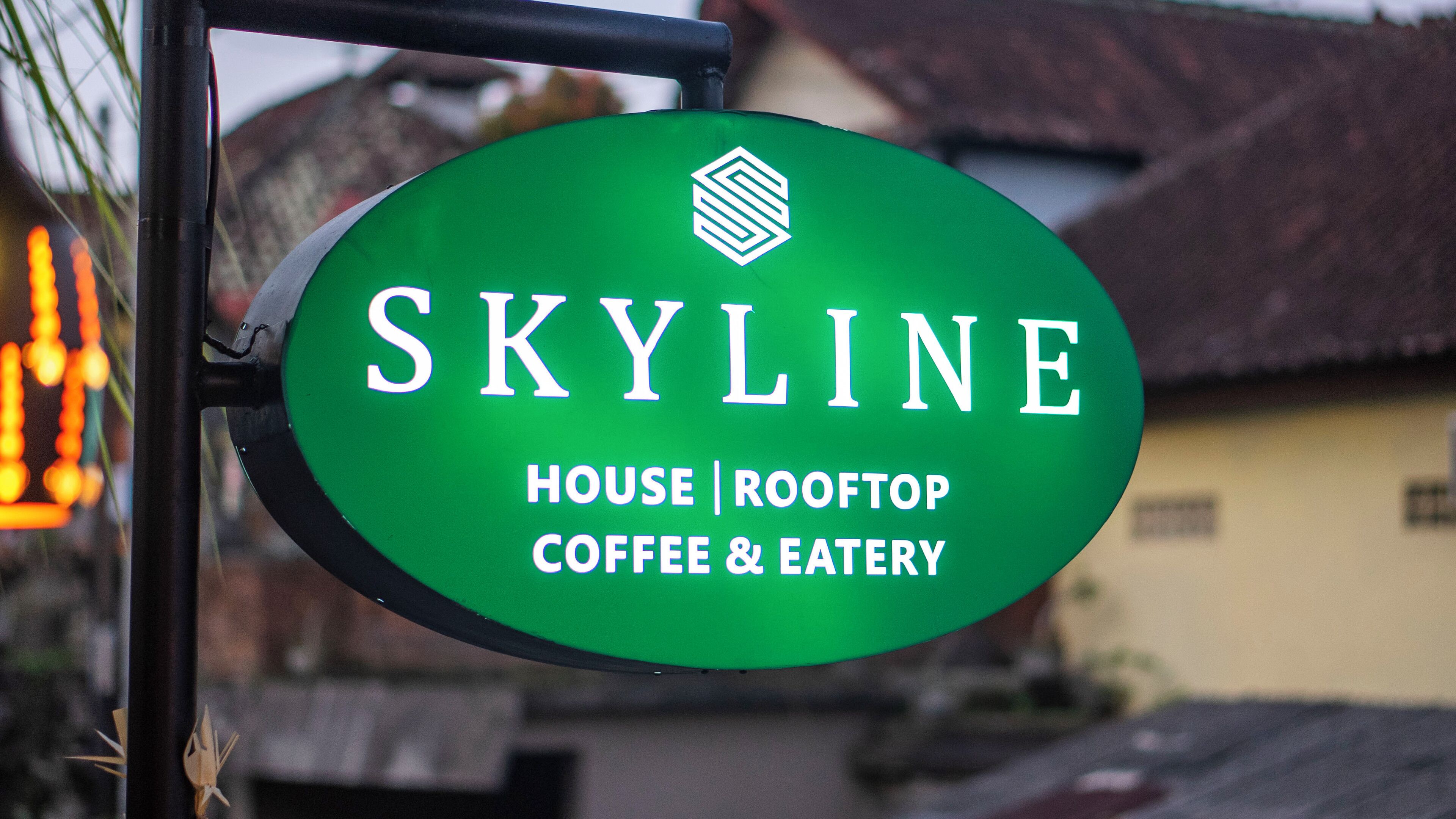 A green sign with the name "SKYLINE" and the words "HOUSE | ROOFTOP | COFFEE & EATERY" indicating a rooftop coffee and eatery.