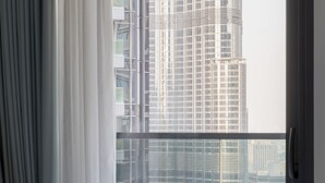 Een hotelkamer met een bed, een raam met gordijnen en uitzicht op hoge gebouwen.