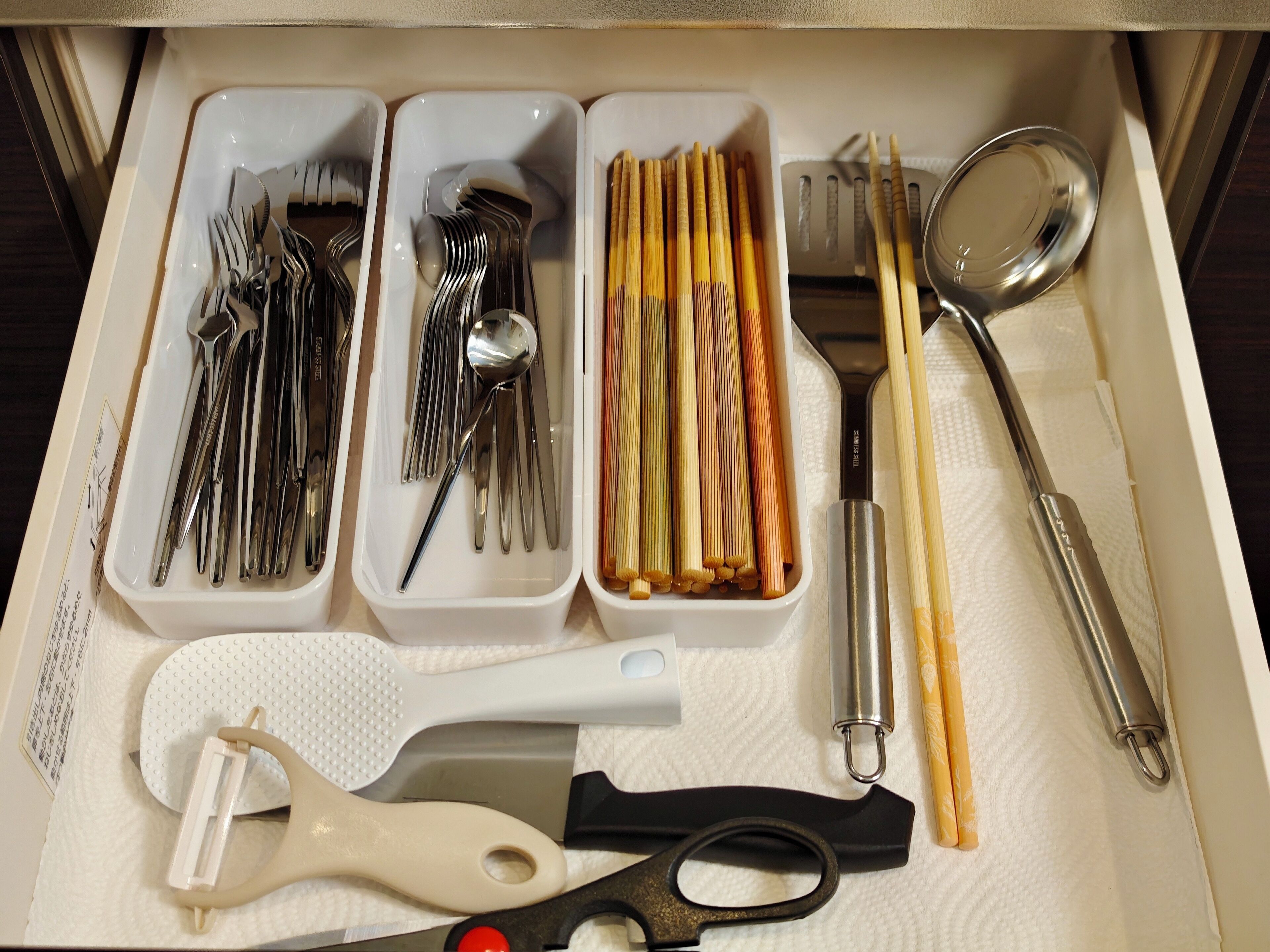 Un cajón con varios utensilios de cocina, incluyendo tenedores, cucharas, palillos y un par de tijeras.