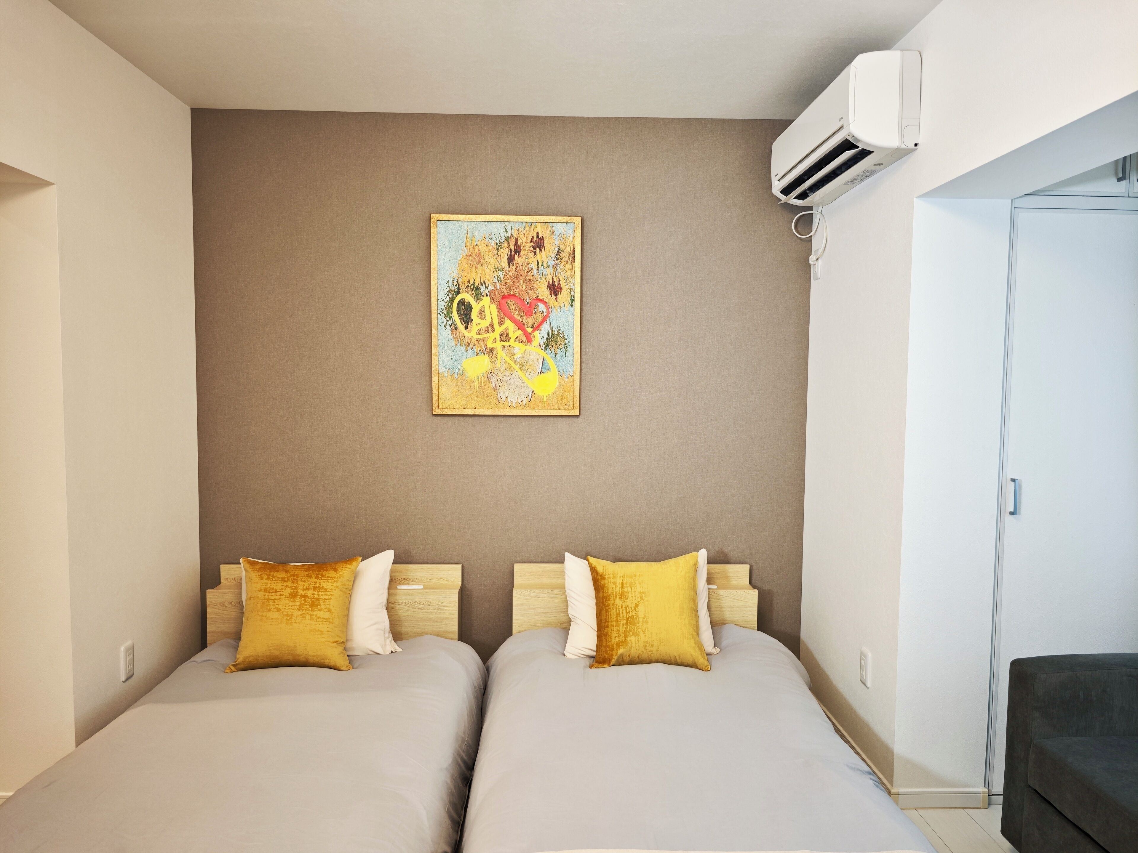 A hotel room with two beds, a wall-mounted air conditioner, and a colorful abstract painting.