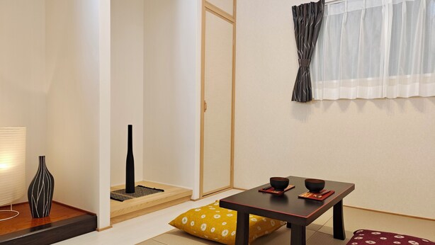 A traditional Japanese room with tatami flooring, a low table with two bowls, a black vase, and a yellow pillow. - K-icon Hotels Chikusa (Nagoya)