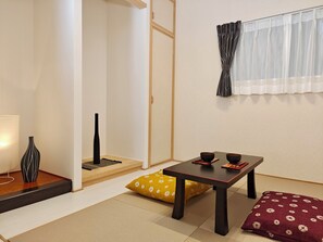 Um quarto japonês tradicional com piso de tatame, uma mesa baixa com duas tigelas, um vaso preto e uma almofada amarela.
