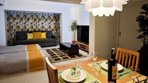 A modern living room with a sofa, television, dining table with chairs, and a decorative ceiling light. - K-icon Hotels Chikusa (Nagoya)