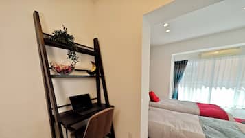 A bedroom with a bed, a desk with a laptop, and a shelf with a plant and decorative items.