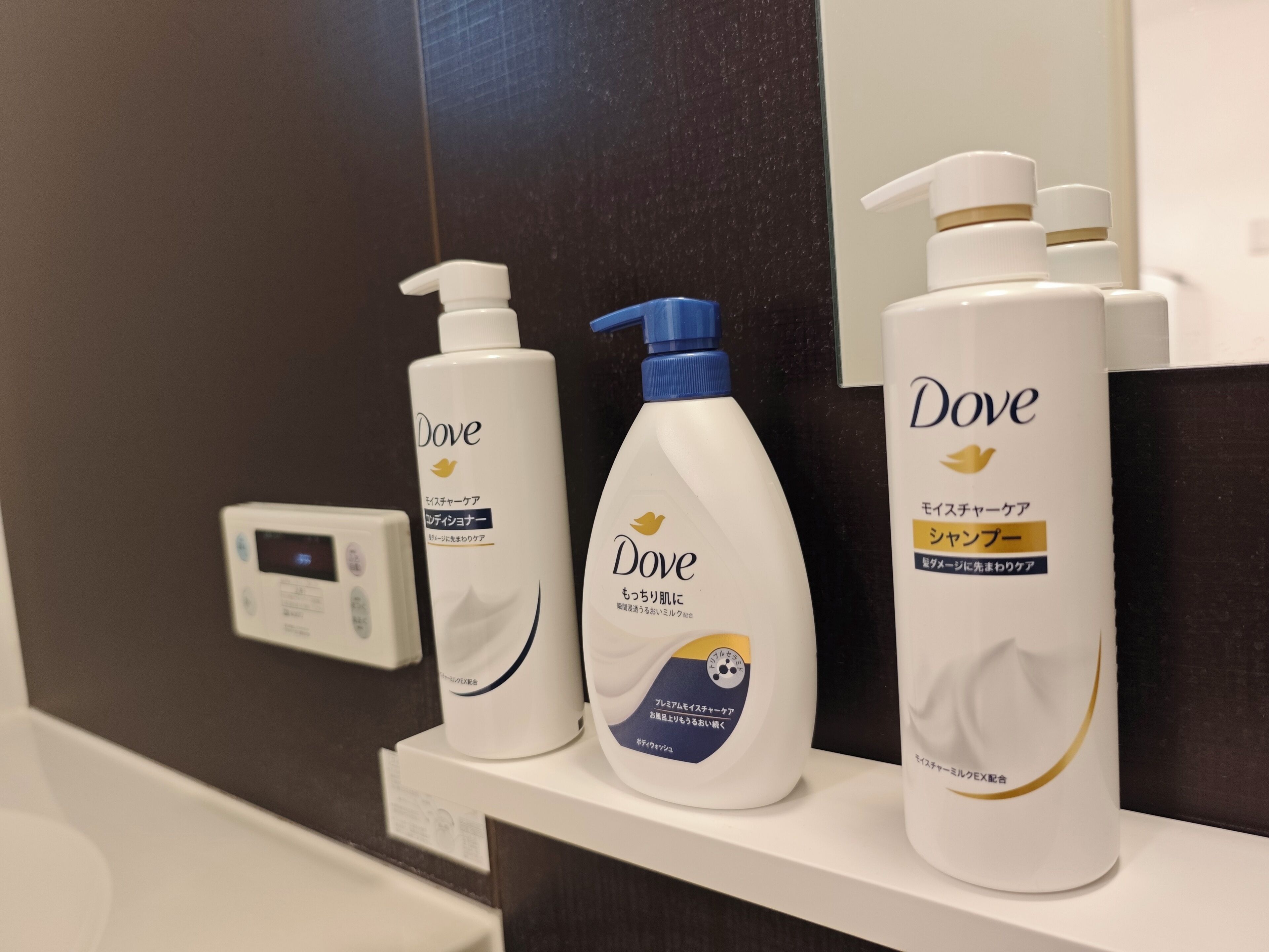 Τρία προϊόντα περιποίησης δέρματος της Dove τοποθετημένα σε ένα λευκό ράφι σε ένα μπάνιο.