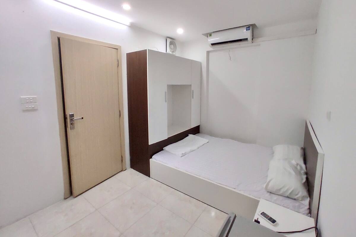 A small, clean room with a bed, a wardrobe, a mirror, and an air conditioning unit.