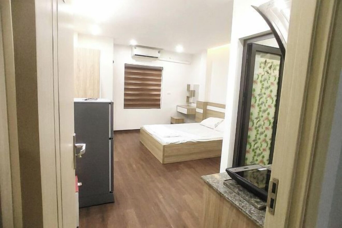 A compact bedroom with a bed, a small desk, a wardrobe, and a window with blinds.