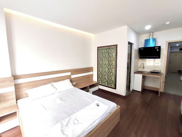 Habitación de hotel con cama, escritorio, televisor y baño visible a través de una puerta abierta.