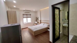 Un dormitorio con cama, armario, ventana y baño visible a través de una puerta abierta.