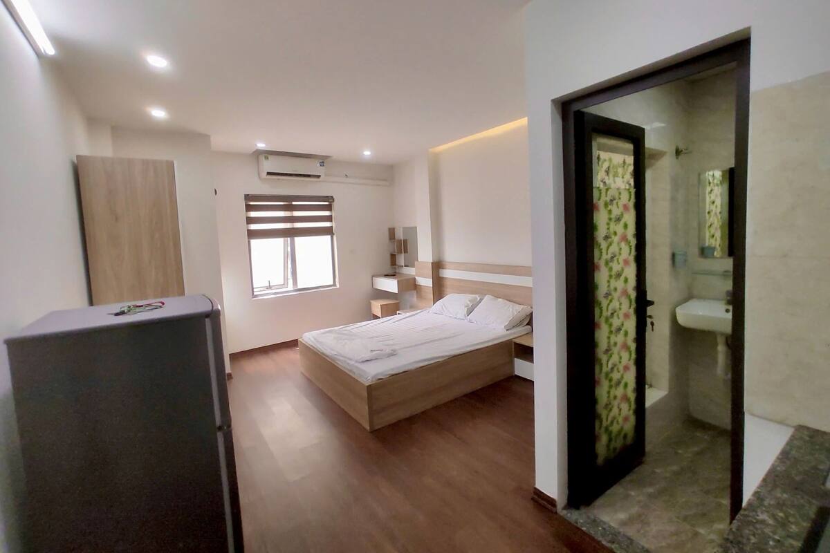 A bedroom with a bed, a wardrobe, a window, and a bathroom visible through an open door.
