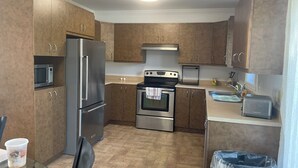 A compact kitchen with stainless steel appliances, wooden cabinets, and a tiled floor. - Home away from home (Saint-Philippe)