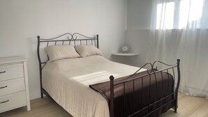 A neatly made bed with a metal frame, a bedside table with a clock, and a white dresser. - Home away from home (Saint-Philippe)
