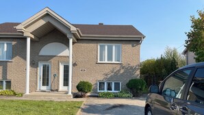 A two-story house with a brick exterior, a front door, a garage door, and a driveway. - Home away from home (Saint-Philippe)