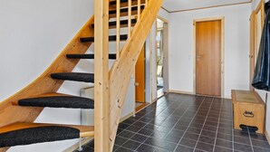 Eine Holztreppe mit schwarzen, rutschfesten Stufen führt zu einem Raum mit Fliesenboden und einer Holztür.