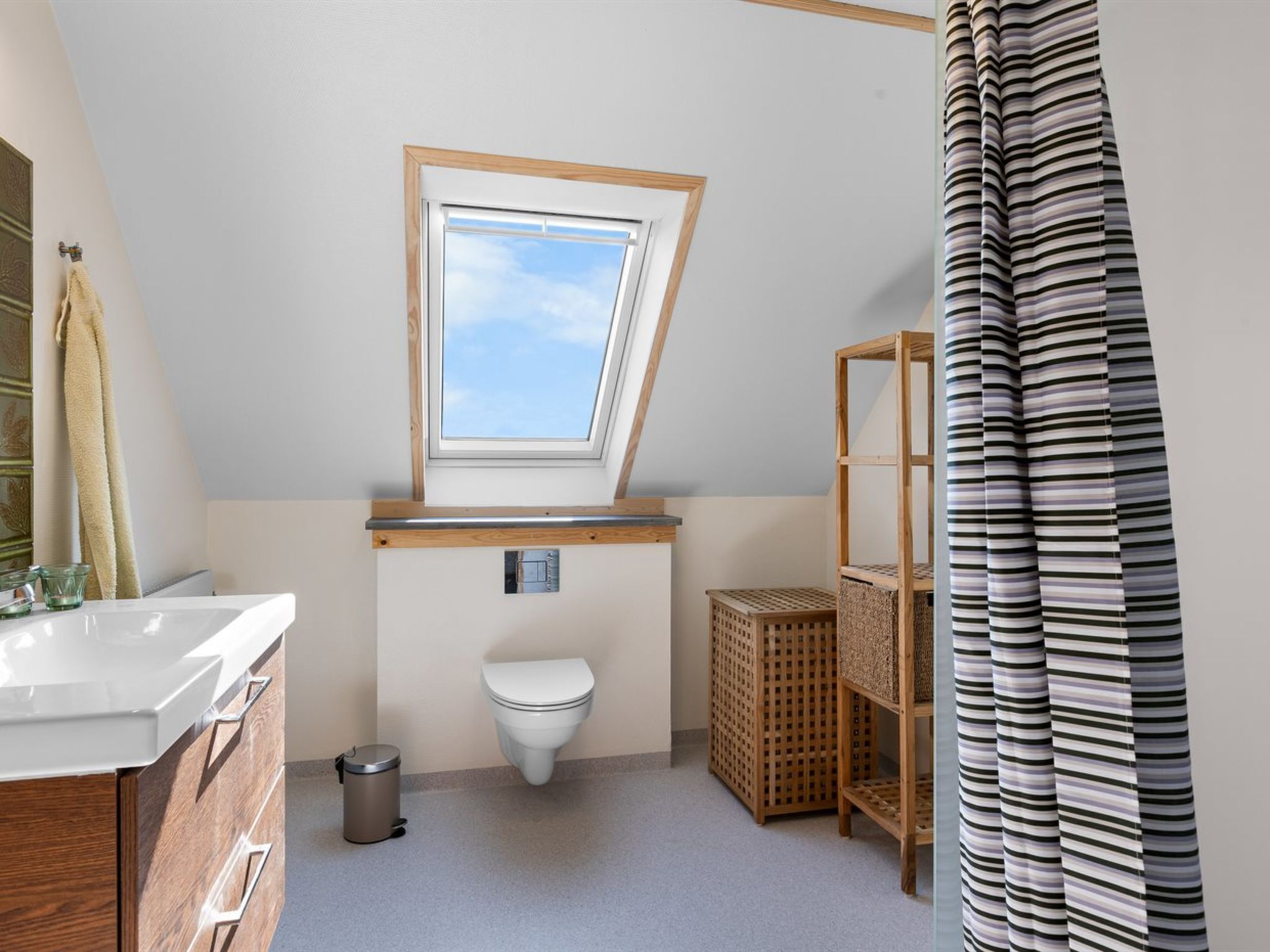 Een kleine, moderne badkamer met dakraam, toilet, wastafel en douchegordijn.