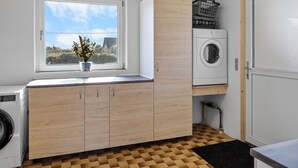 Ein Waschraum mit Waschmaschine, Trockner, Holzausstattung, einem Fenster mit Blick ins Grüne und einem Fliesenboden.