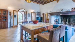 A rustic kitchen with a wooden table, chairs, and a fireplace. - Podere Palazzetto by Interhome (Buonconvento)