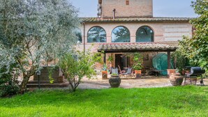 A rustic villa with a brick facade, large arched windows, and a covered patio area with outdoor furniture. - Podere Palazzetto by Interhome (Buonconvento)