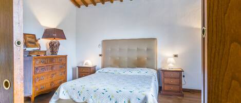 Um quarto com cama, cómoda de madeira, mesas de cabeceira e um tapete estampado.